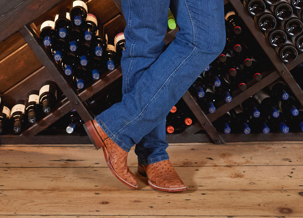 A man wearing Justin Western Boots while standing in front of a wine rack.